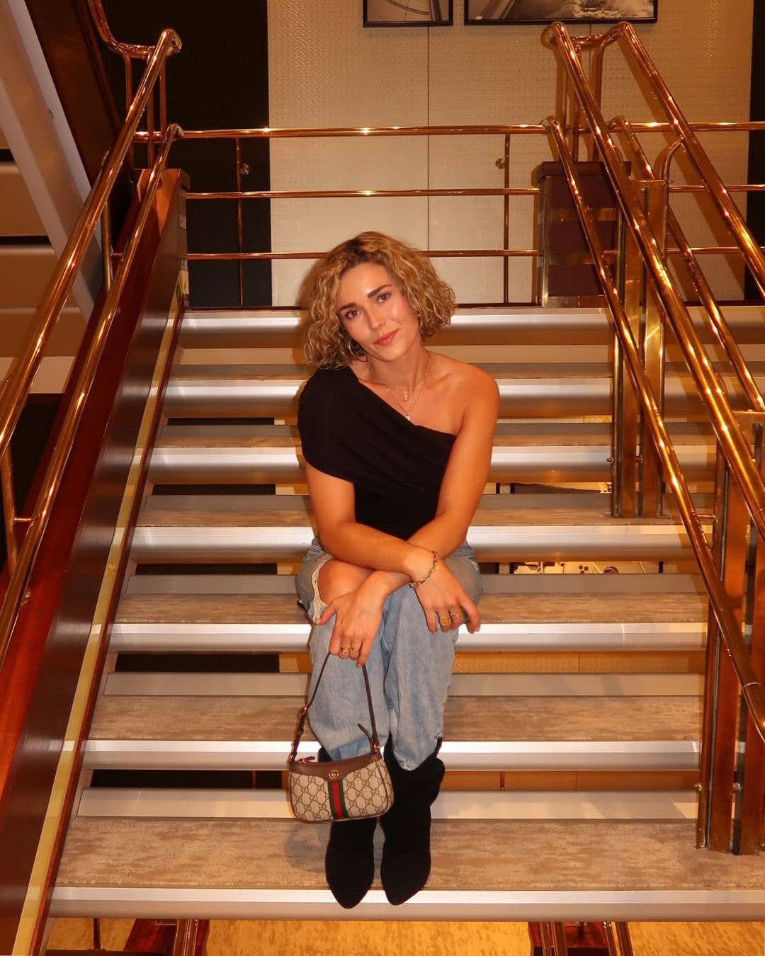 Schwarze NOELLE Stiefel zu heller Jeans und schwarzem Top, getragen im Sitzen auf einer Treppe
